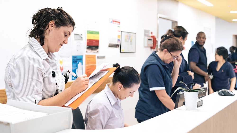 Hospital staff at desk and woman holding folder