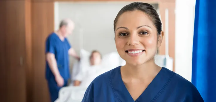 Ethnic nurse in front of hospital bed smiling at camera 