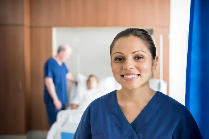 Ethnic nurse in front of hospital bed smiling at camera 